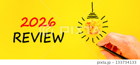 2026 Review symbol. Concept words 2026 Review on beautiful yellow paper. Beautiful orange paper background. Light bulb icon. Businessman's hand with pen. Business and 2026 review concept. Copy space. 2026 Review symbol. Concept words 2026 Review on beautiful yellow paper. Beautiful orange paper background. Light bulb icon. Businessman's hand with pen. Business and 2026 review concept. Copy space. 133734133