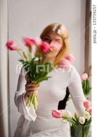 Elegant blonde woman gazing amidst tulip arrangement in studio 133734257