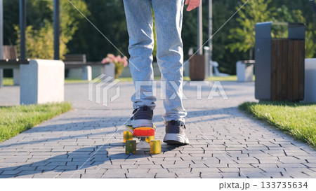 Rear view of girl skateboarding on a pathway heading to school in casual clothes carrying a pink schoolbag enjoying the sunny morning Rear view of girl skateboarding on a pathway heading to school in casual clothes carrying a pink schoolbag enjoying the sunny morning 133735634