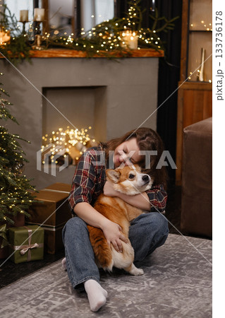 Caucasian woman sitting with corgi dog in cozy Christmas room with warm lights and tree 133736178