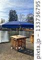 Cozy Outdoor Bar Tables Under a Blue Umbrella By a Serene Pond Setting for Relaxed Weekend Leisure 133736795