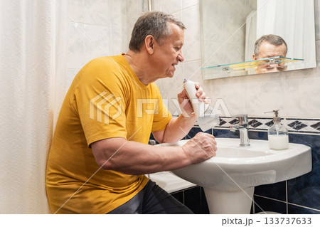 Cleaning teeth with oral irrigator after brushing, caucasian adult male performing advanced oral hygiene at bathroom sink. Man Brushing Teeth Cleaning teeth with oral irrigator after brushing, caucasian adult male performing advanced oral hygiene at bathroom sink. Man Brushing Teeth 133737633