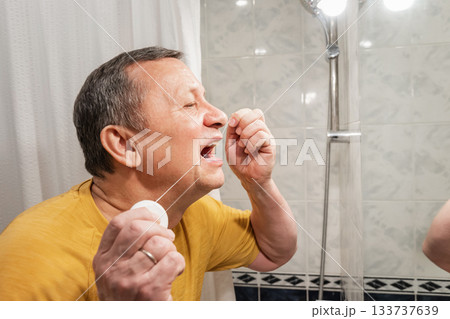 Using dental floss for interdental cleaning, caucasian adult male performing oral hygiene routine at bathroom mirror. Man Brushing Teeth 133737639