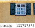 A charming vintage window with green wooden shutters on a textured yellow wall, capturing warm architectural detail and rustic European character. 133737878