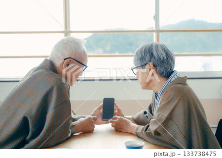 旅館の和室でスマホを一緒に眺める高齢夫婦 133738475