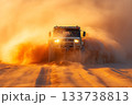 Heavy offroad truck charging through dense desert dust with headlights cutting through the haze 133738813