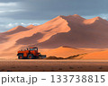 Large loader moving sand at the base of towering orange dunes under soft afternoon light 133738815