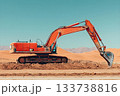 Bright orange excavator digging into dry desert soil with mountains and dunes in the background 133738816