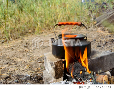 black camping kettle heating on an open fire in nature 133738874