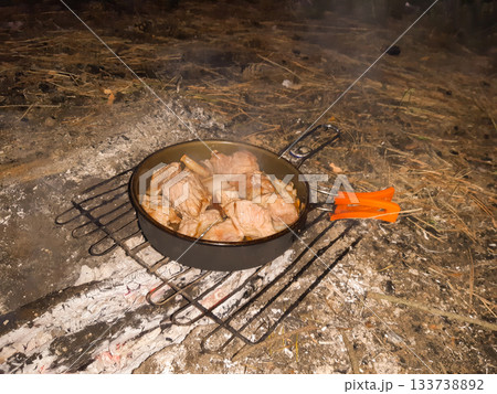 top view of pieces of meat and lard in a camping pan over smoldering coals top view of pieces of meat and lard in a camping pan over smoldering coals 133738892