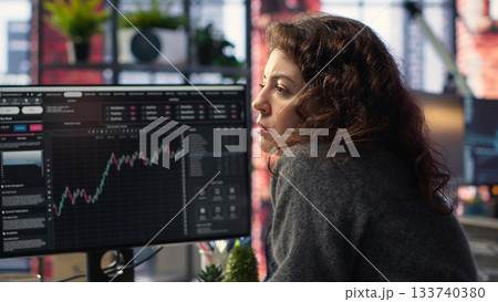 Businesswoman studies financial charts using stock market visualization tools. Digital trading platform provides economic data, forex analysis and price trends for investment planning. Camera B. 133740380