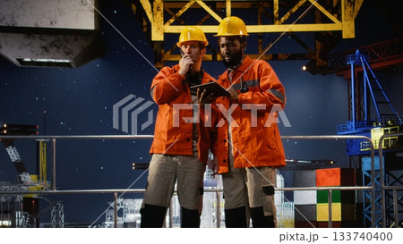 Industrial workers communicating via radio devices performing inspection and monitoring duties on offshore platform rig, supporting gasoline and oil production within the industry. Industrial workers communicating via radio devices performing inspection and monitoring duties on offshore platform rig, supporting gasoline and oil production within the industry. 133740400