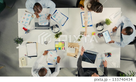 Top down view of employees reviews documentation and performance reports. Colleagues in a professional office setting collaborate on planning, projections and market research. 133740434