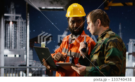 Soldier in uniform operate communication devices during a maritime mission with engineer, providing security for offshore platform logistics and drilling rig protection operations. 133740438