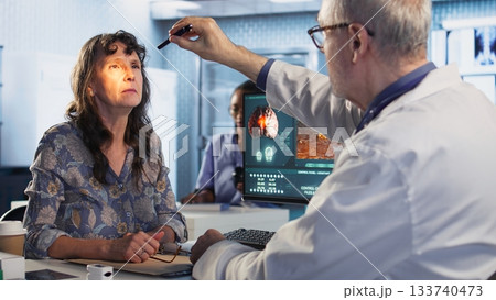 Healthcare expert man conducting a concussion test with pen light in cabinet, evaluating the woman focus, coordination and pupil reaction after a suspected head trauma. Camera A. Healthcare expert man conducting a concussion test with pen light in cabinet, evaluating the woman focus, coordination and pupil reaction after a suspected head trauma. Camera A. 133740473