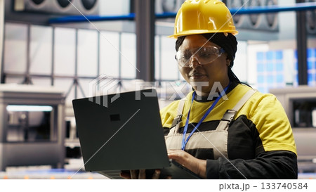 Industrial plant engineer using laptop to implement automated workflows and control systems, computerizing operations. African american technician integrates sensors into production using notebook Industrial plant engineer using laptop to implement automated workflows and control systems, computerizing operations. African american technician integrates sensors into production using notebook 133740584