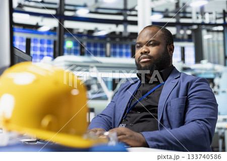 Male factory consultant observes production systems on a pc in a solar plant, providing expert feedback on efficiency, safety and sustainability aligned with green energy initiatives. 133740586