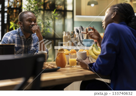 African american lovers chatting over their coffee at the breakfast table, enjoying free weekend morning at home and relaxing together. Young man and woman enjoy a chill lifestyle. 133740632
