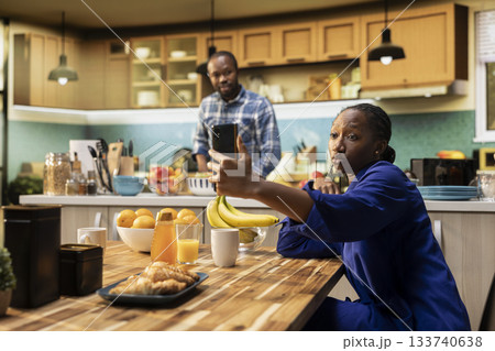 African american woman takes selfies on her smartphone and acting silly, boyfriend laughing at her and enjoying a cute funny moment together on a weekend morning. Relaxation at home. 133740638