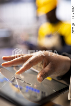 Closeup of technician leveraging a digital app to enhance solar energy output. Selective focus on factory specialist using tablet, supervising smart machinery used in solar panel production. Closeup of technician leveraging a digital app to enhance solar energy output. Selective focus on factory specialist using tablet, supervising smart machinery used in solar panel production. 133740640