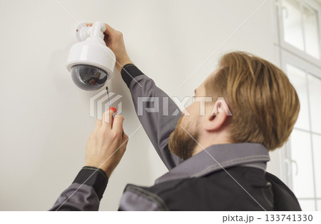 CCTV wall installation connecting dome camera, worker setting up system for viewing and recording 133741330