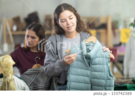 Young girl choosing light green vest for autumn-winter in clothing store Young girl choosing light green vest for autumn-winter in clothing store 133742389