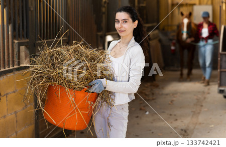 Young woman with bucket of hay in stable 133742421