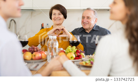 Elderly parents showing love gesture at family dinner with children 133742725