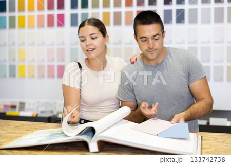In store, couple buyer look at product catalog and choose color of paint, wall covering in apartment In store, couple buyer look at product catalog and choose color of paint, wall covering in apartment 133742738