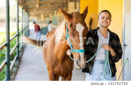 Young woman leading horse out of stable 133742756