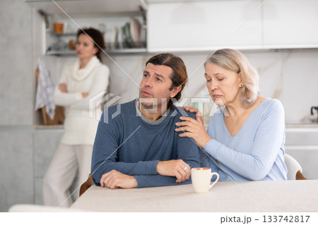 Senior woman sits near adult son and comforts him during quarrel with wife. 133742817