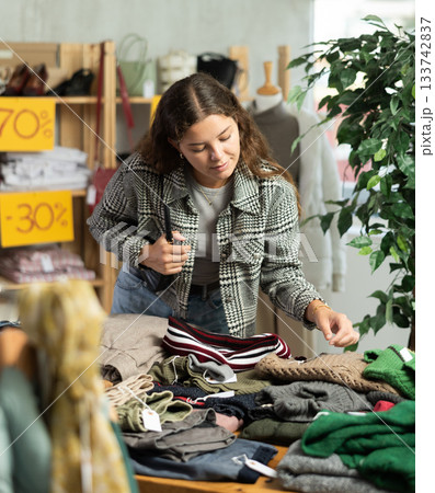 Young woman chooses sweater in clothing store Young woman chooses sweater in clothing store 133742837