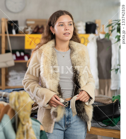 During November sales, young woman choose and try on fur coat, view reflection in mirror. During November sales, young woman choose and try on fur coat, view reflection in mirror. 133742839