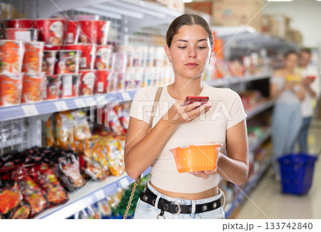 Female shopper scans qr code with smartphone on label of chinese noodles in supermarket Female shopper scans qr code with smartphone on label of chinese noodles in supermarket 133742840
