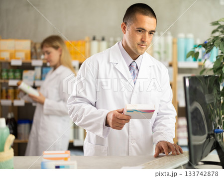 male pharmacist working on a computer in a pharmacy male pharmacist working on a computer in a pharmacy 133742878