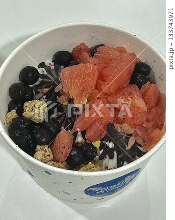Swirled yogurt ice cream dessert served in a cup, smooth creamy texture with glossy surface, topped with fresh fruit pieces, highlighting its refreshing and inviting appearance in detail Swirled yogurt ice cream dessert served in a cup, smooth creamy texture with glossy surface, topped with fresh fruit pieces, highlighting its refreshing and inviting appearance in detail 133743971