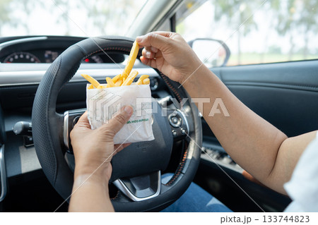 Asian lady holding French fries potato chips to eat in car, dangerous and risk an accident. 133744823