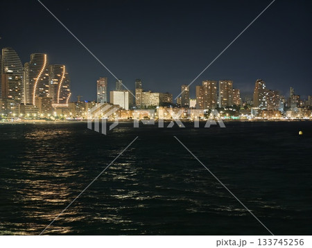 calm bay under city lights, quiet night scene featuring skyline reflections and gentle waves 133745256