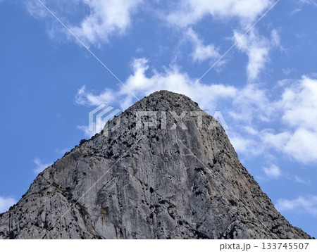 rugged peak with clouds and shadows, towering rocky summit piercing clouds with raw texture 133745507