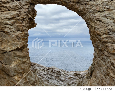 windblown waves crash against rocky shoreline beneath brooding overcast sky and distant horizon 133745728