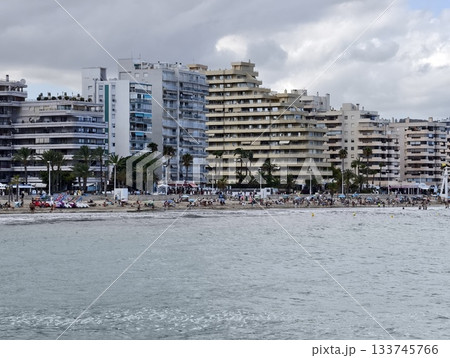 crowded shoreline with tourism activity, bustling sandy beach promenade featuring sunbathers 133745766