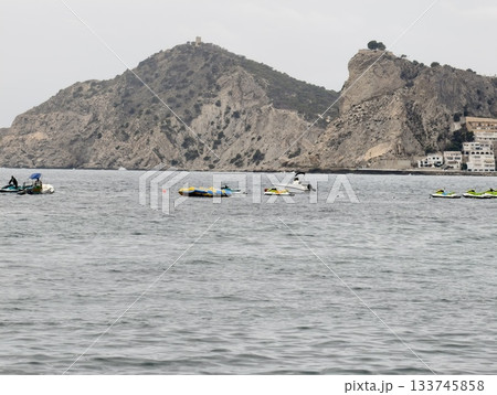 coastal paddlers enjoying calm waters, tourists gather near shoreline with kayaks and serene sky 133745858