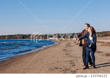 Young carefree couple in love throwing pebbles, shells, stones into sea outdoors. Fun family game together. High quality photo 133746125