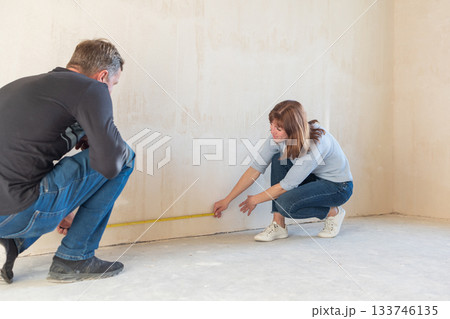Young couple moving in new apartmen. People measure size of wall with tape measure. Concept new homes, new beginning. High quality photo Young couple moving in new apartmen. People measure size of wall with tape measure. Concept new homes, new beginning. High quality photo 133746135