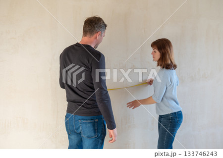 Young couple moving in new apartmen. People measure size of wall with tape measure. Concept new homes, new beginning. High quality photo 133746243