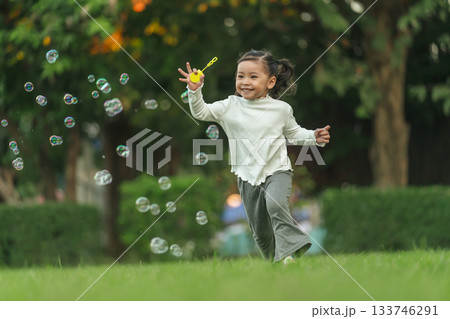 happy toddler girl running and playing soap bubble in park 133746291