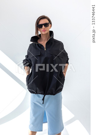 Elegant woman in black windbreaker jacket and light blue skirt on white background. Fashionable female style. Studio photography. Vertical photo. High quality photo 133746441