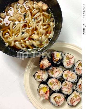 Kimbap rolls neatly sliced with colorful fillings beside a steaming bowl of udon noodles, highlighting vibrant ingredients, soft textures, and comforting appearance in close-up detail Kimbap rolls neatly sliced with colorful fillings beside a steaming bowl of udon noodles, highlighting vibrant ingredients, soft textures, and comforting appearance in close-up detail 133747633