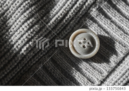 Detailed view of a button on a gray knitted garment. Detailed view of a button on a gray knitted garment. 133750843