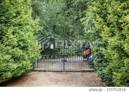 A black iron gate stands between dense green walls, silent under the weight of summer air. A black iron gate stands between dense green walls, silent under the weight of summer air. 133752616